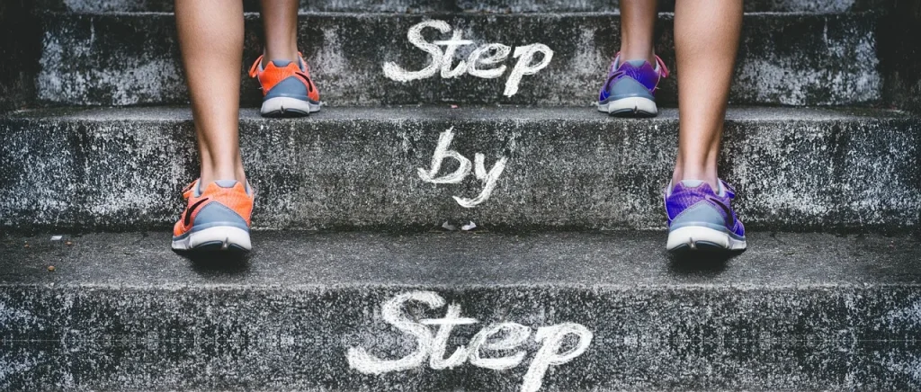 Two people in colorful sneakers climbing concrete stairs painted with the words Step by Step